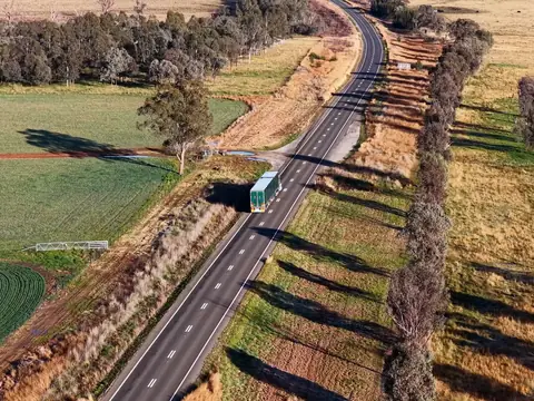 Aerial view of a truck with two plain green trailers travelling in the left lane of a country highway between paddocks and gum trees