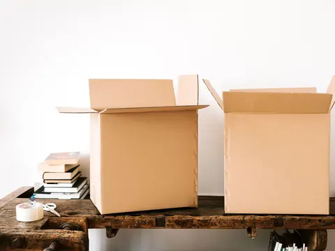Two open, empty cardboard boxes on an old wooden bench beside a stack of books and a roll of tape