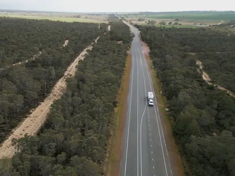 Aerial view of a sealed country highway running straight through dense mallee scrub towards open farmland