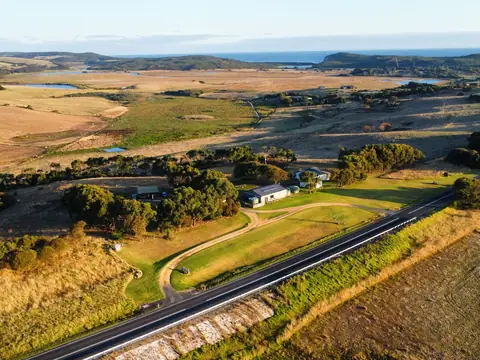 Aerial view of a highway running past farmland, scattered trees and a farmhouse towards the coast